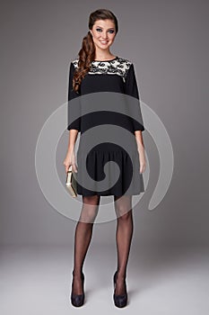 Beautiful young business woman with evening make-up wearing a dress and high-heeled shoes and a small black handbag, business