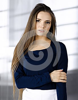 Beautiful young business woman with long hair or female student urban dressed is standing straight and posing at camera