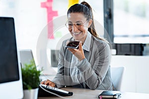 Beautiful young business woman using smart phone while working with her computer in the office