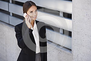 Beautiful young business woman is walking by a building while talking on the phone