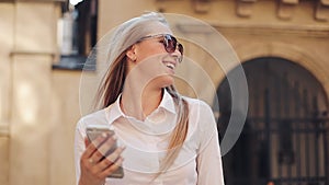 Beautiful young business woman wearing white shirt and using smartphone while walking in the city center summer internet