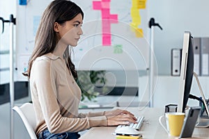 Beautiful young business woman working with computer while sitting in desk in modern startup office