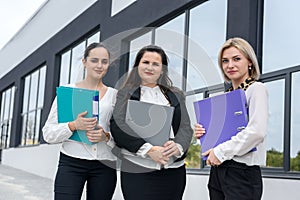 Beautiful and young business women with documents and folders posing outside office building