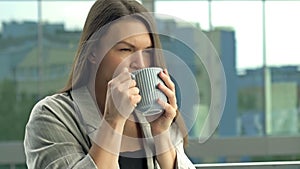 Beautiful young businesswoman drinking hot tea or coffee while standing on the office balcony.