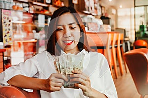 Beautiful young businesswoman happily counts banknotes in a coffee shop.