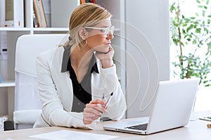 Beautiful young businesswoman looking sideways while working with her laptop in the office.