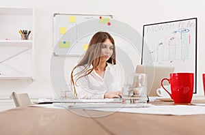 Beautiful young businesswoman sitting by office desk with laptop