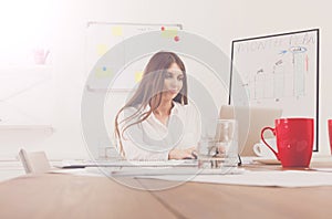 Beautiful young businesswoman sitting by office desk with laptop