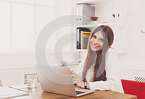 Beautiful young businesswoman sitting by office desk with laptop