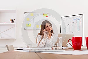 Beautiful young businesswoman sitting by office desk with laptop