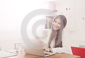 Beautiful young businesswoman sitting by office desk with laptop