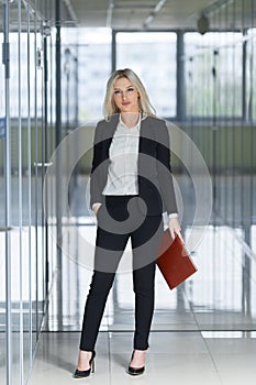 Beautiful young businesswoman standing with folder in the office.