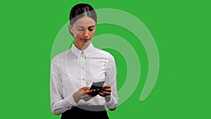 Beautiful, young businesswoman standing and typing on her phone, isolated on green background