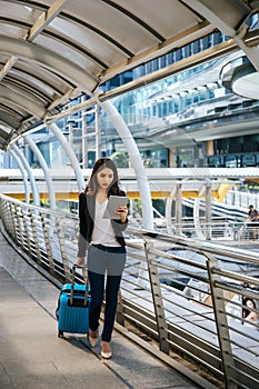 Beautiful young businesswoman walking outside public transportation station. Businesswoman traveler with suitcase on the way to