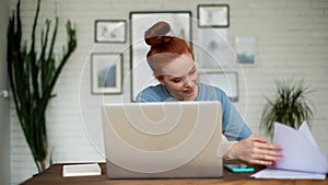 Beautiful young businesswoman is writing in documents while working on laptop.
