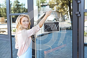 beautiful young cafe owner holding sign open and smiling