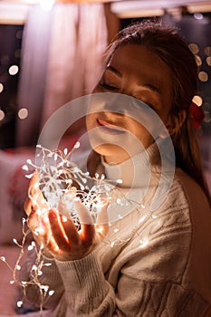 Beautiful young candid woman holding in hands near the face a bright led garland of glowing lights and enjoyment an inspiring mood