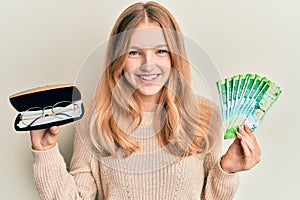 Beautiful young caucasian girl holding glasses and russian ruble banknotes smiling and laughing hard out loud because funny crazy