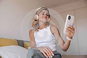 Beautiful young caucasian girl is looking for music on phone to listen to headphones.