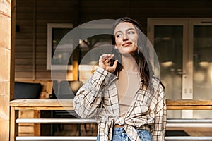 Beautiful young caucasian girl poses looking away standing near cottage outside city.