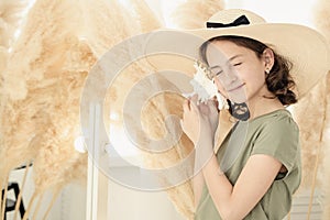 Beautiful young caucasian girl in a straw hat with a white seashell. The girl closed her eyes and listens to the sound of the sea