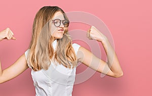 Beautiful young caucasian girl wearing casual clothes and glasses showing arms muscles smiling proud