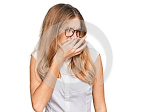 Beautiful young caucasian girl wearing casual clothes and glasses smelling something stinky and disgusting, intolerable smell,