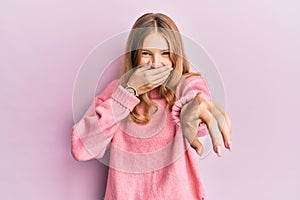 Beautiful young caucasian girl wearing casual clothes laughing at you, pointing finger to the camera with hand over mouth, shame