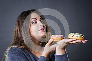 Beautiful young caucasian plus size model posing with donuts on a gray studio background photo