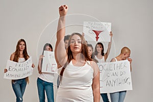 Beautiful young caucasian plus size woman in white shirt raised her arm, looking at camera. Group of diverse women