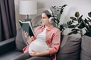 Beautiful young Caucasian pregnant woman listen to music with wireless headphone and reading book to tell story to unborn child.