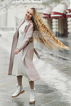 beautiful young caucasian smiling woman in beige coat with long hair walking outdoors,