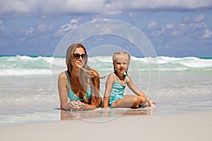 Beautiful young caucasian woman in blue bikini and little girl on the sandy beach. Summer family vacations, travel