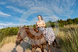 Beautiful young Caucasian woman cantering atop a brown horse in a lush green field.