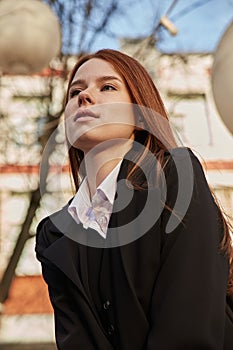 beautiful young caucasian woman in coat with long hair sitting outdoors at park