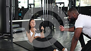 Beautiful young caucasian woman are doing crunches at the gym under the guidance of a fitness instructor african man