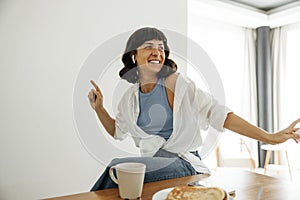 Beautiful young caucasian woman having fun listening to music in headphones at breakfast in morning.