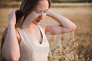 Beautiful young caucasian woman with long blond hair touching her hair on a background of a wheat field
