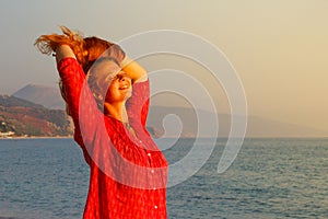 A beautiful young Caucasian woman in a pink blouse with red hair smiles and enjoys the sunset against the background of the Medite