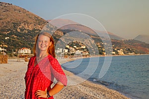 A beautiful young Caucasian woman in a pink blouse with red hair smiles and enjoys the sunset against the background of the Medite