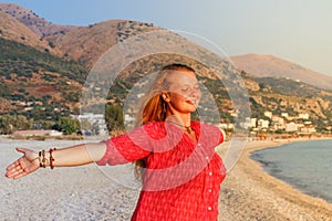 A beautiful young Caucasian woman in a pink blouse with red hair smiles and enjoys the sunset against the background of the Medite