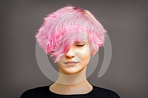 Beautiful young caucasian woman with short curly bob hairstyle dyed in pink color with closed eyes against dark gray