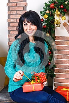 Beautiful young caucasian woman sitting in a Christmas interior, holds a red gift box.