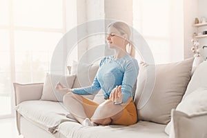 Beautiful young caucasian woman sitting in yoga lotus zen position and meditating. Concept relax on sofa living room