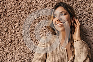 Beautiful young caucasian woman smiles teeth looking away against background of grey wall.