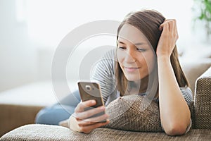 Beautiful young caucasian woman on sofa using cell phone