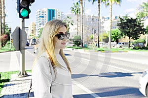 Beautiful young caucasian woman waiting for traffic lights to cross the road on the city street background. Lifestyle photo.