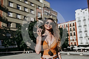 Beautiful young caucasian woman walking at the city street on a sunny day. Sending an audio with mobile phone. Happy face smiling