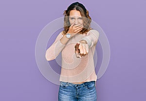 Beautiful young caucasian woman wearing casual sweater laughing at you, pointing finger to the camera with hand over mouth, shame