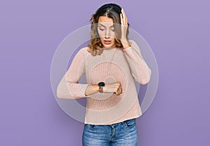 Beautiful young caucasian woman wearing casual sweater looking at the watch time worried, afraid of getting late
